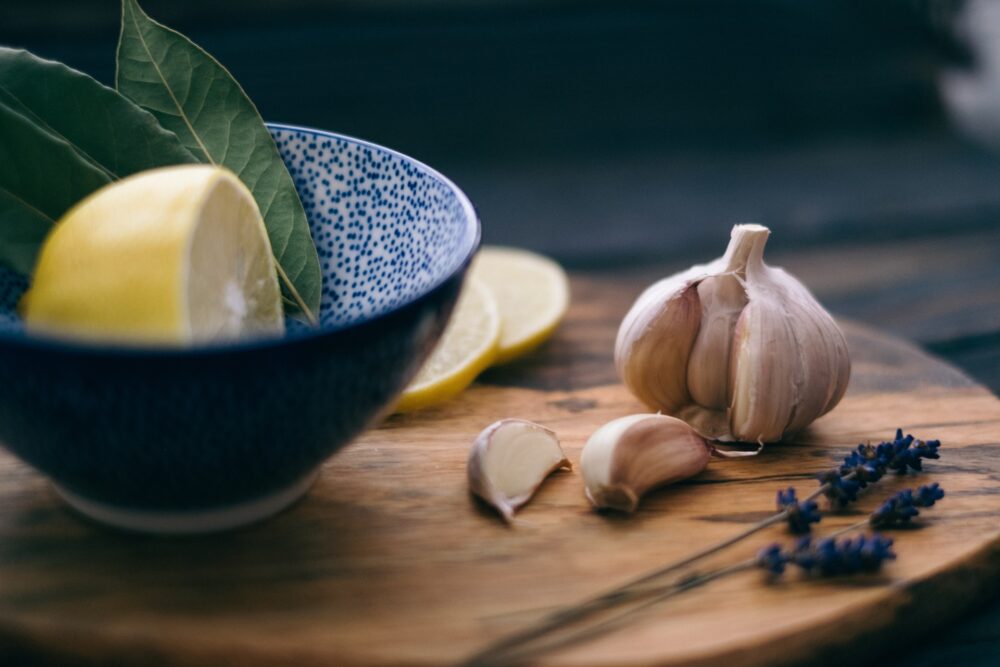 A head of garlic on a cutting board. Beside it, a cut lemon in a speckled bowl