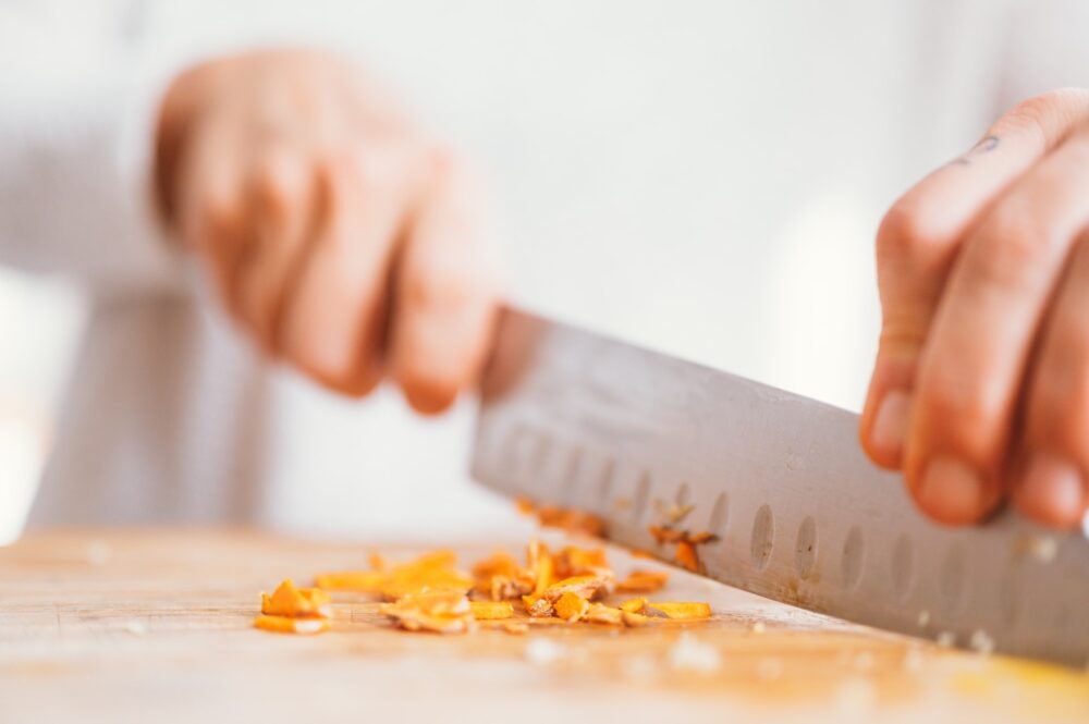 Two hands holding a chef's knife and chopping something orange