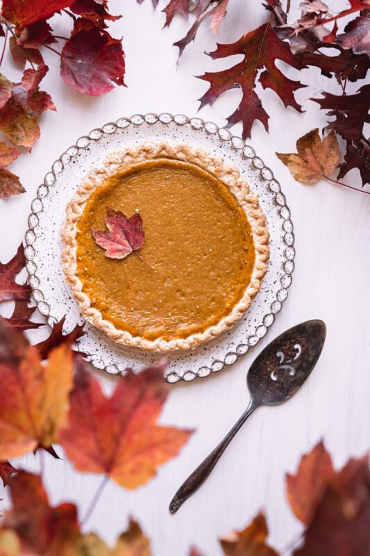 Pumpkin pie on a glass plate surrounded by fall leaves