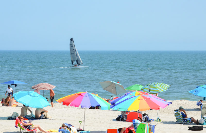 Sailboat off of Howard Beach, colorful beach umbrellas in the foreground