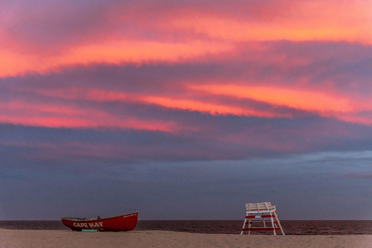 Pink clouds in the sky with a lifeguard stand and "Cape may" lifeguard boat on the beach