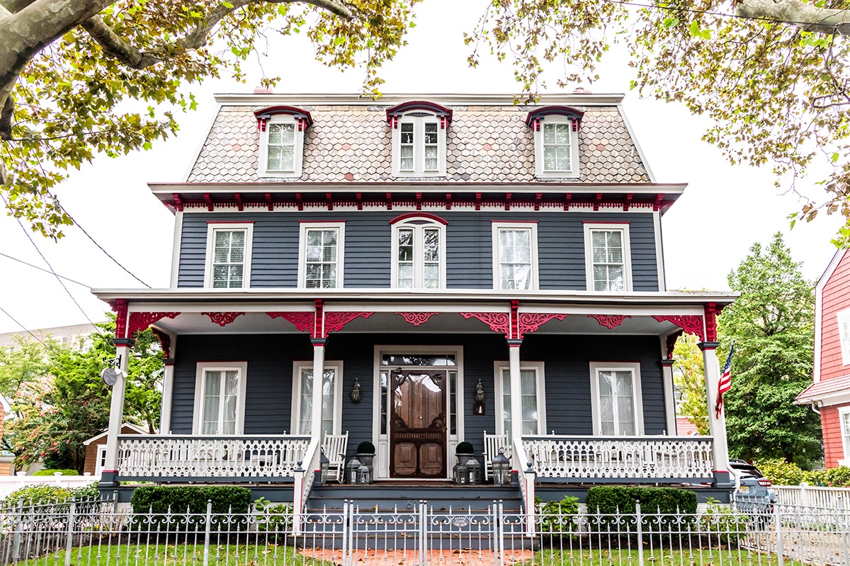 A dark blue-gray Victorian house with red trim on a cloudy day