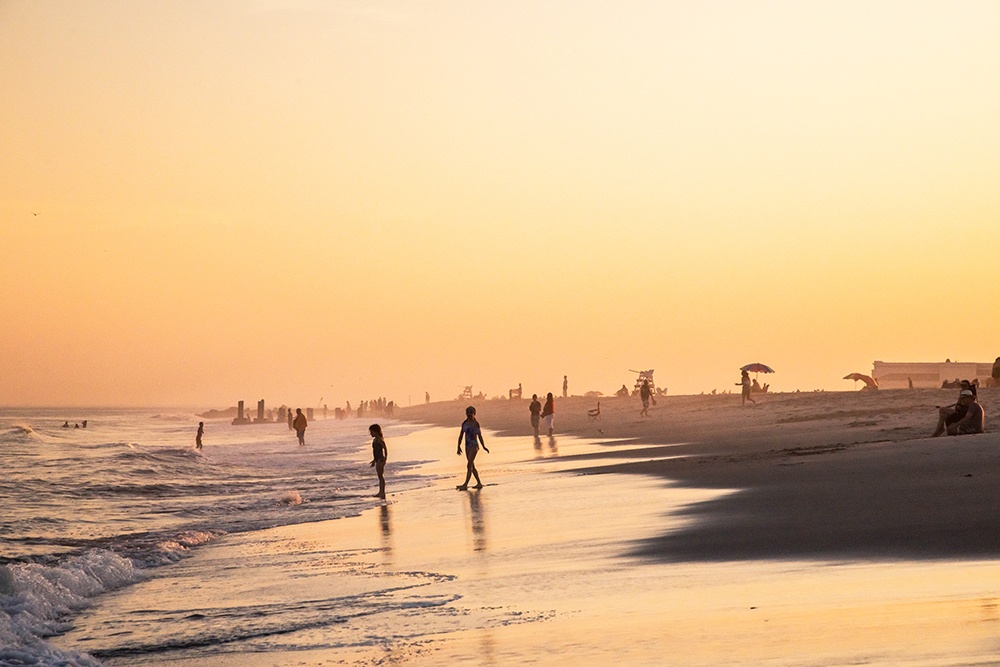 people in the ocean and walking on the beach during a summer sunset