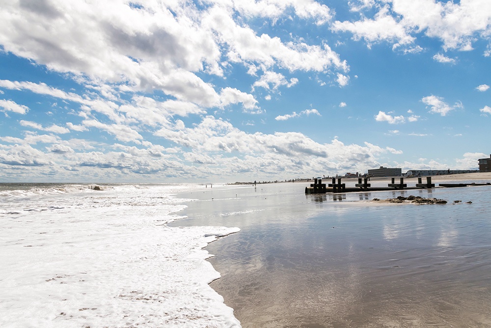 Blue skies with puffy clouds as the ocean crashes into the sand