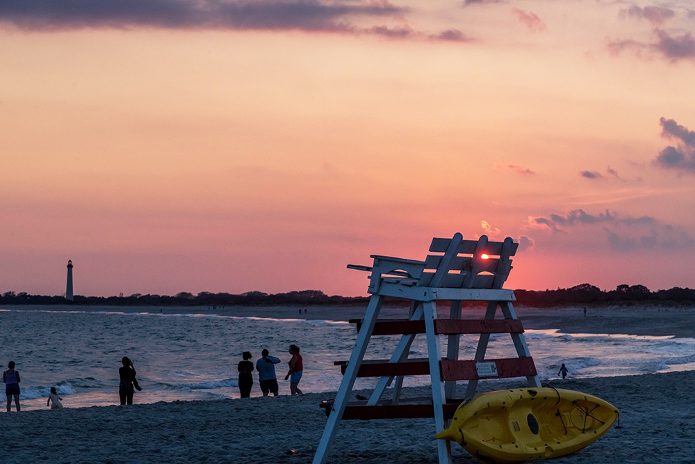 Sun setting behind a lifeguard stand while people stand by the ocean