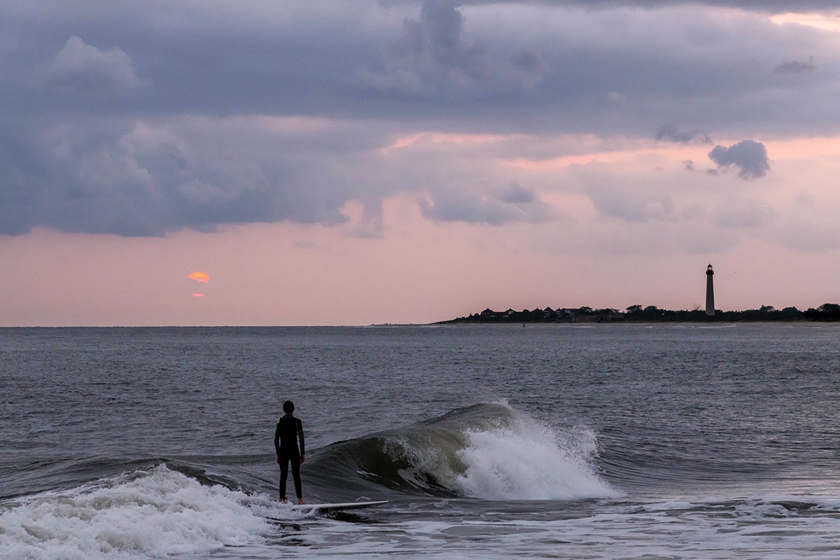 Surfer at sunset with the Cape May lighthouse in the distance