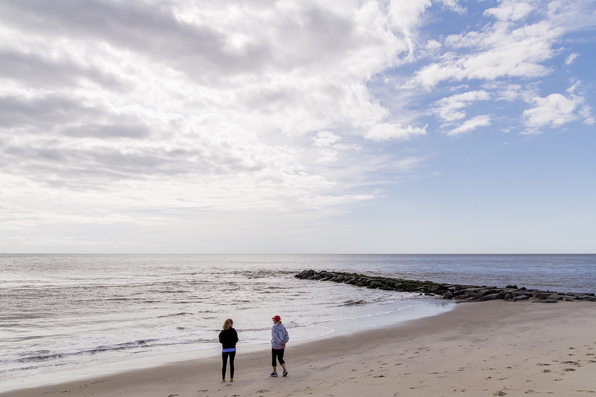 A half blue half cloudy sky with two people standing down by the ocean