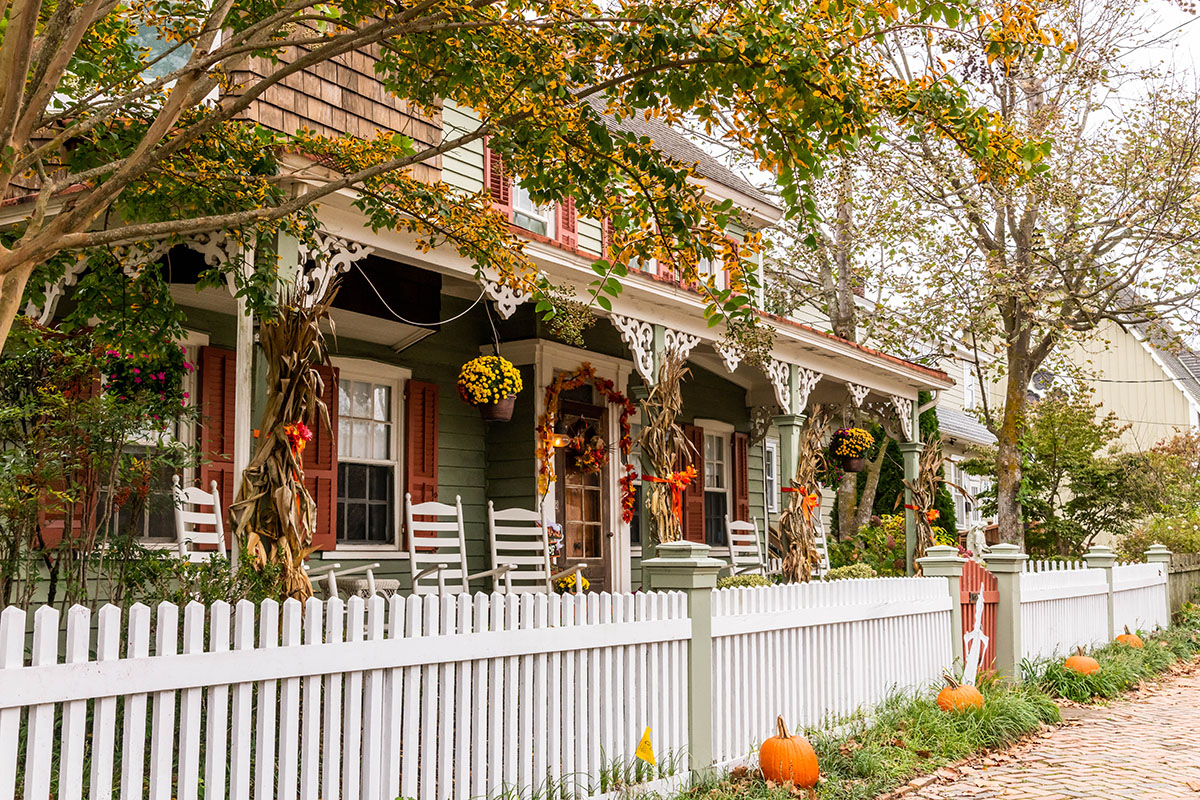 A victorian house with decorated with yellow mums, hay, and pumpkins with a tree with changing leaves