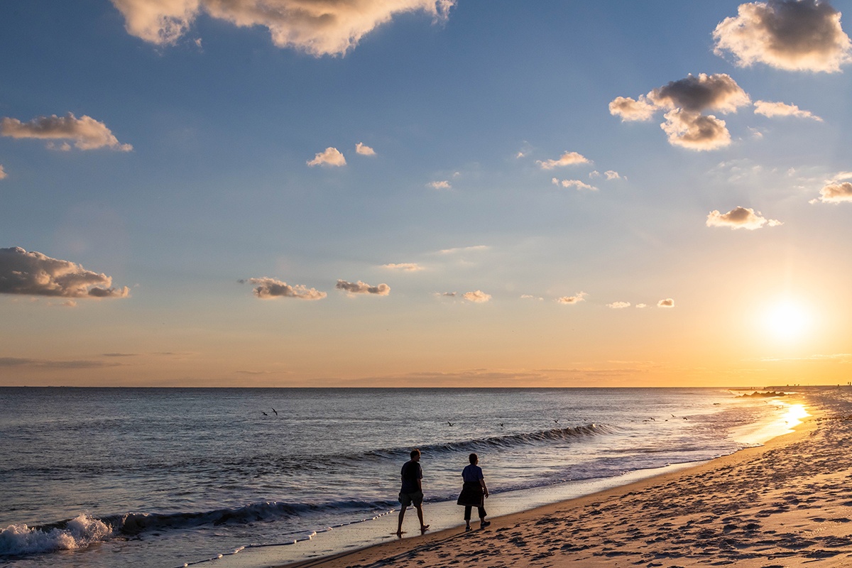 Two people walking on the beach by the ocean at sunset with puffy clouds in the sky