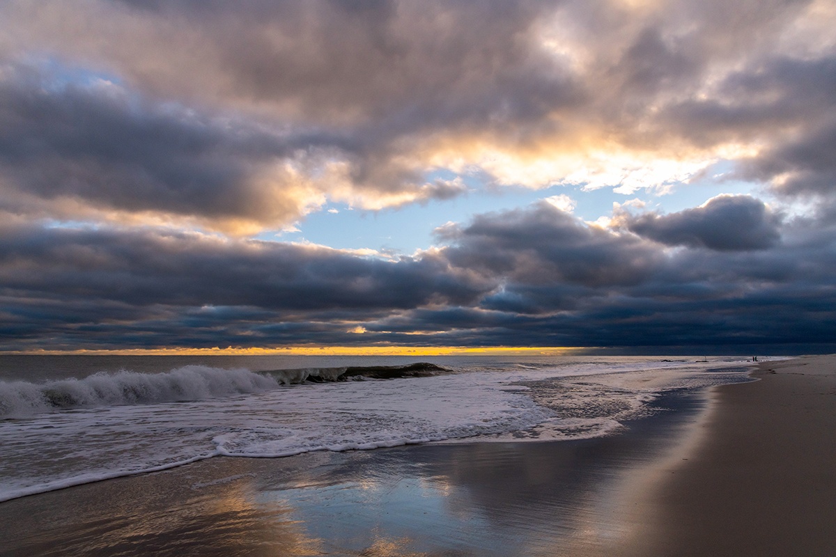 A wave crashing with colorful clouds breaking up in the sky