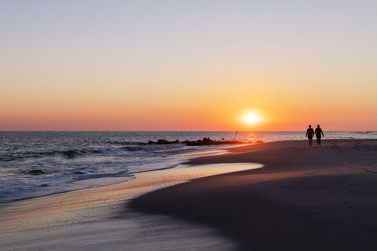 Two people walking by the ocean as the sun sets