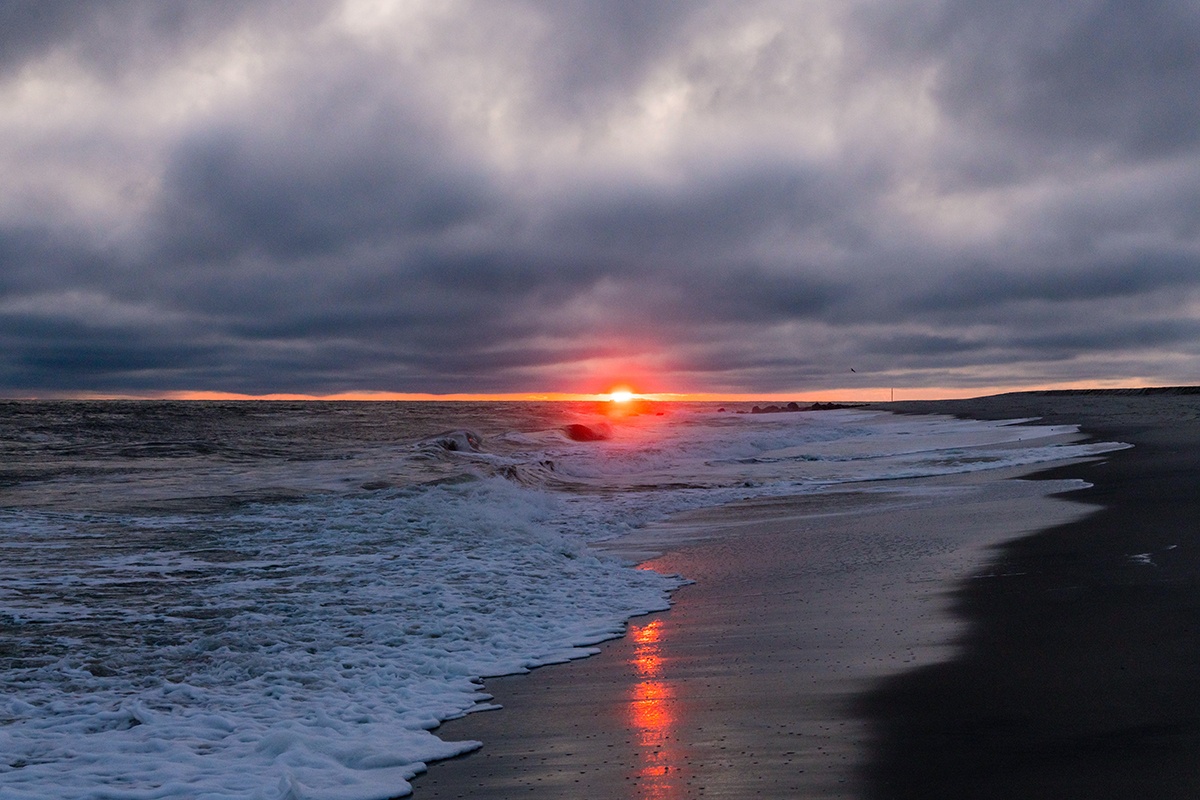 Sun setting at the horizon with clouds in the sky and waves crashing