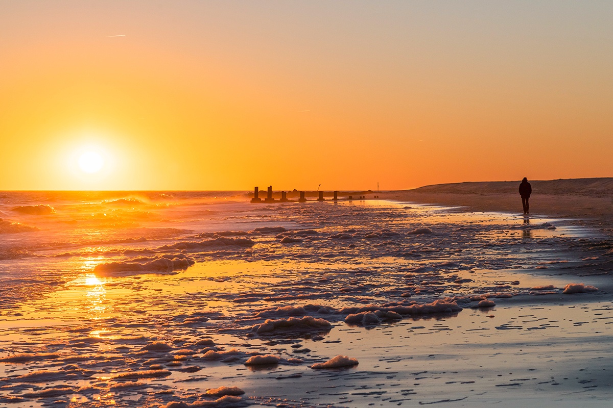 A person walking by the ocean as the sun sets