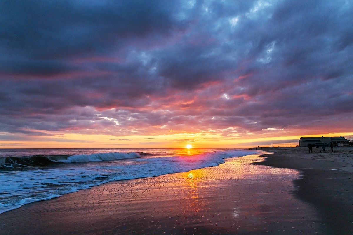 The sun setting with pink clouds in the sky reflected in the sand