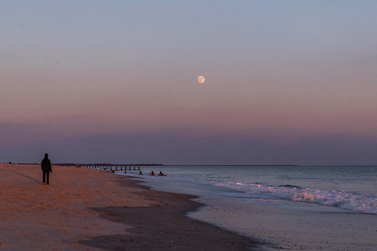 Full moon rising over the ocean with a person walking on the beach