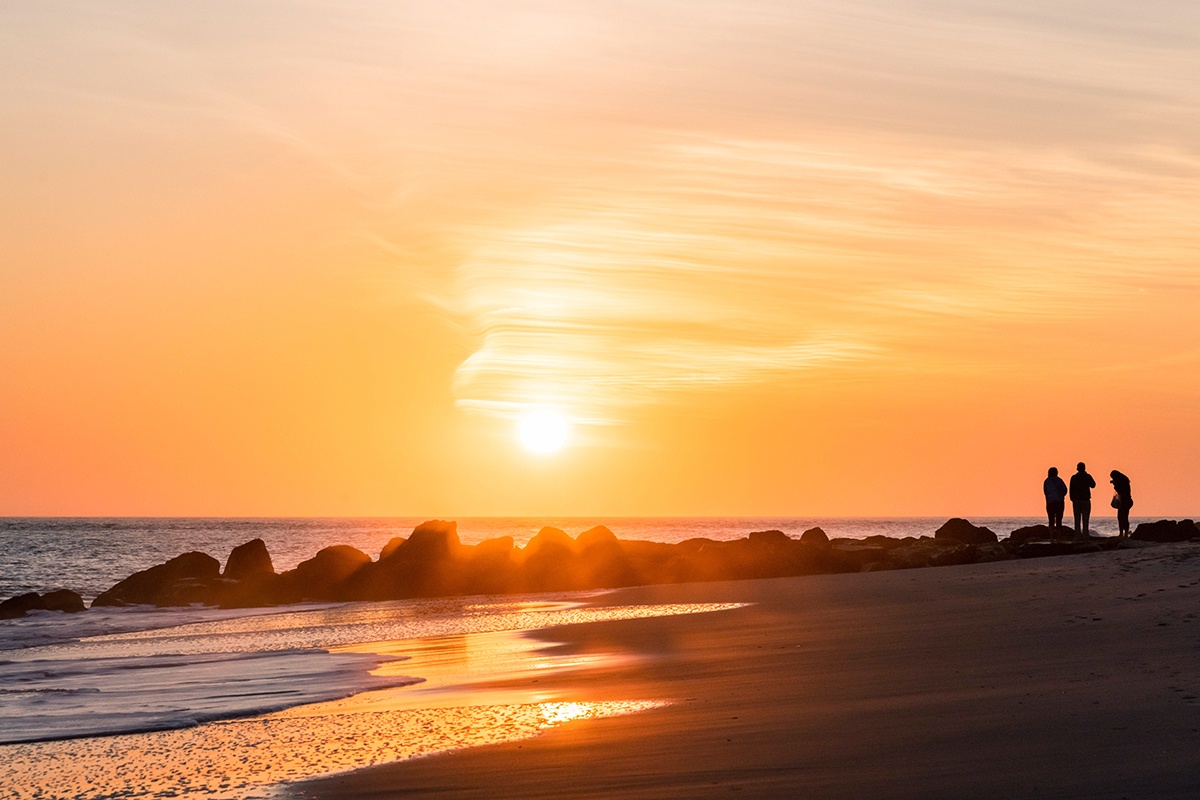 Sun setting at the beach with three people watching on a jetty