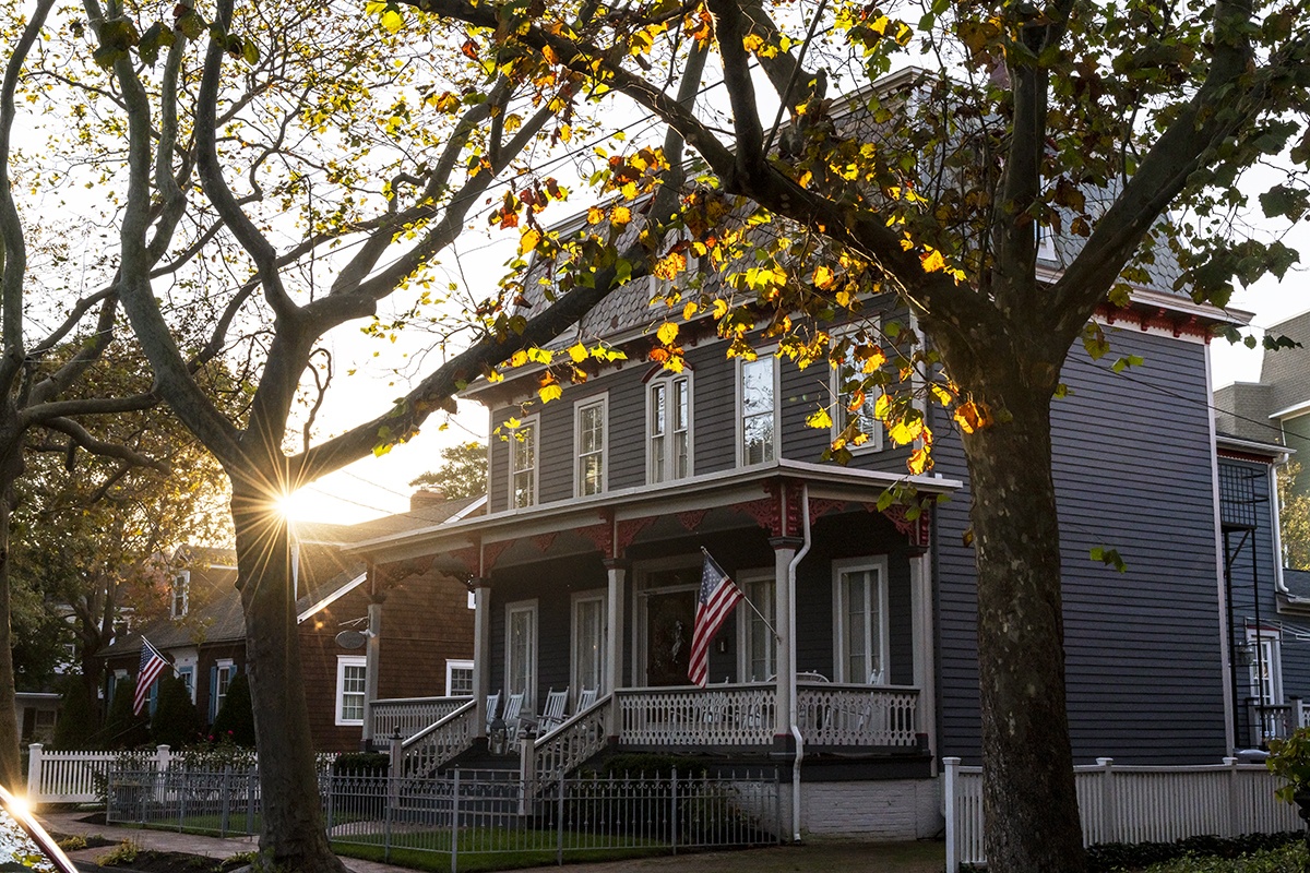 Sun setting behind trees with fall leaves and a Victorian house