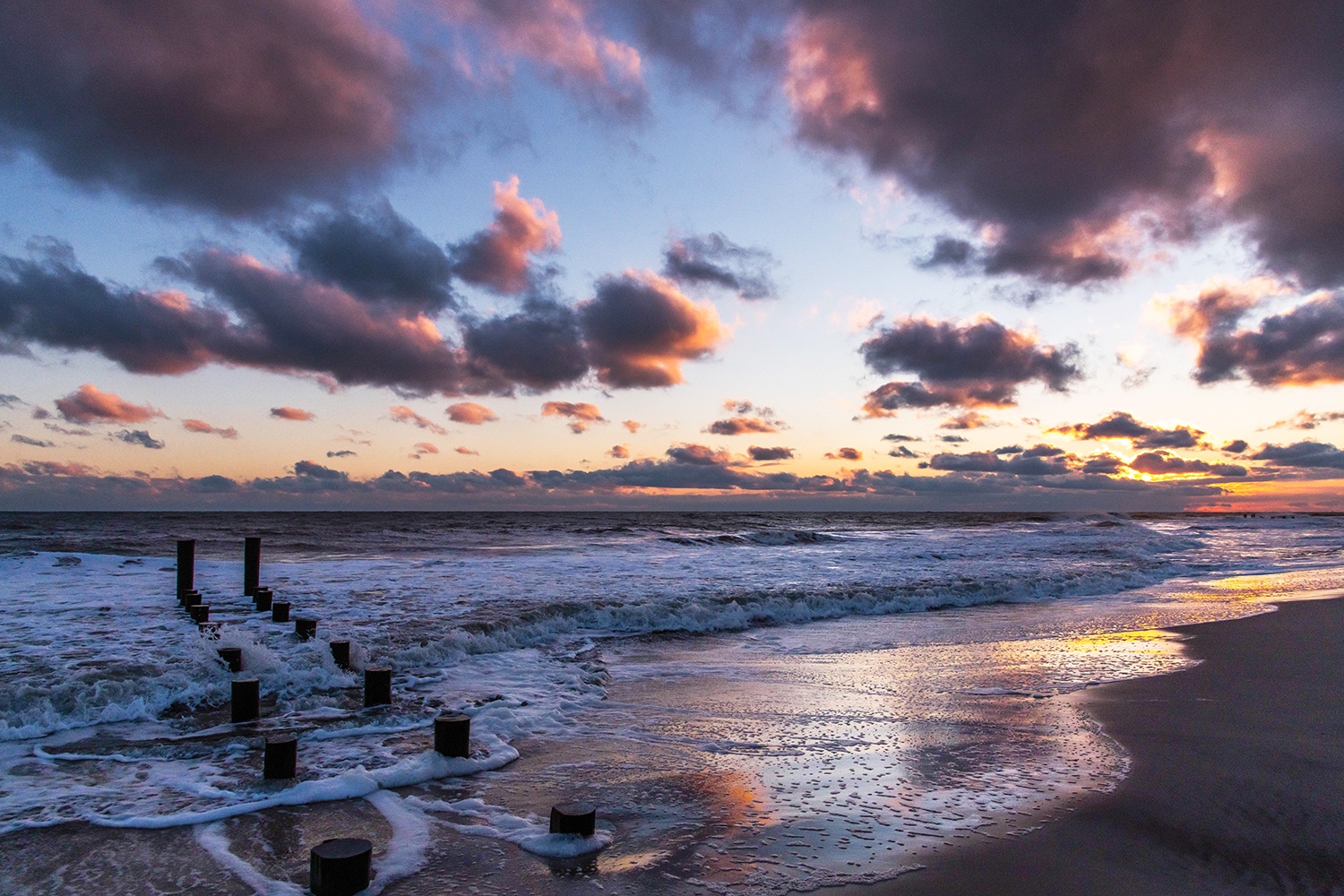 Sunset at the beach with waves crashing and pink and purple puffy clouds