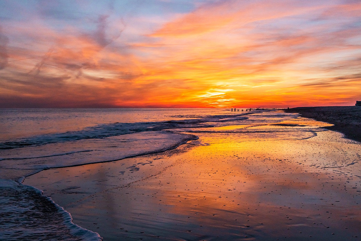 Pink, orange, and red clouds in the sky at sunset reflected in the sand