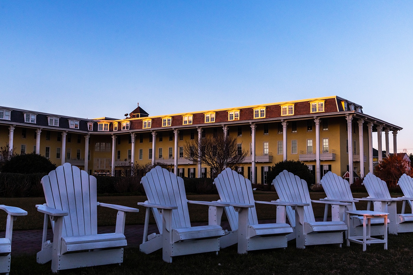 Empty white chairs on the front lawn at Congress Hall with sunlight from sunset hitting the roof