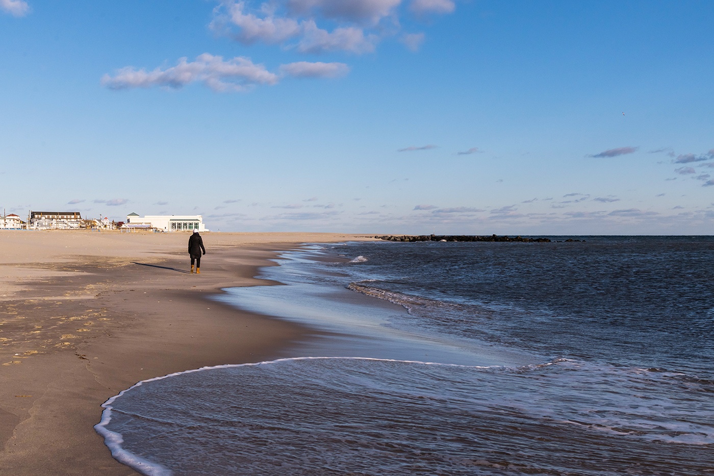 A person walking on the beach by the ocean in the winter on a bright blue sunny day