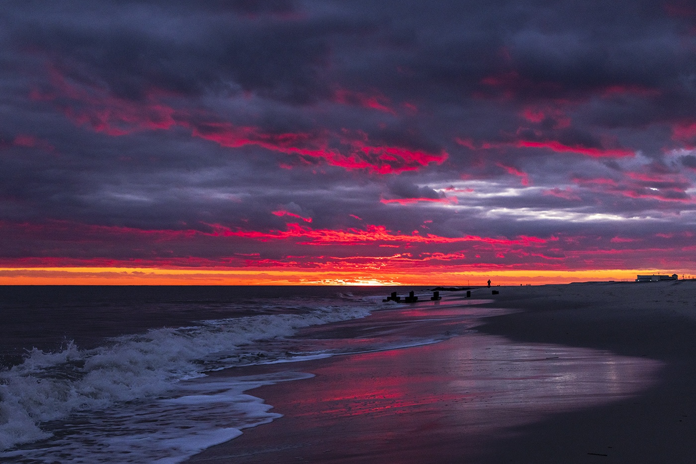 Bright pink colors in the clouds at sunset on a cloudy day with waves crashing 