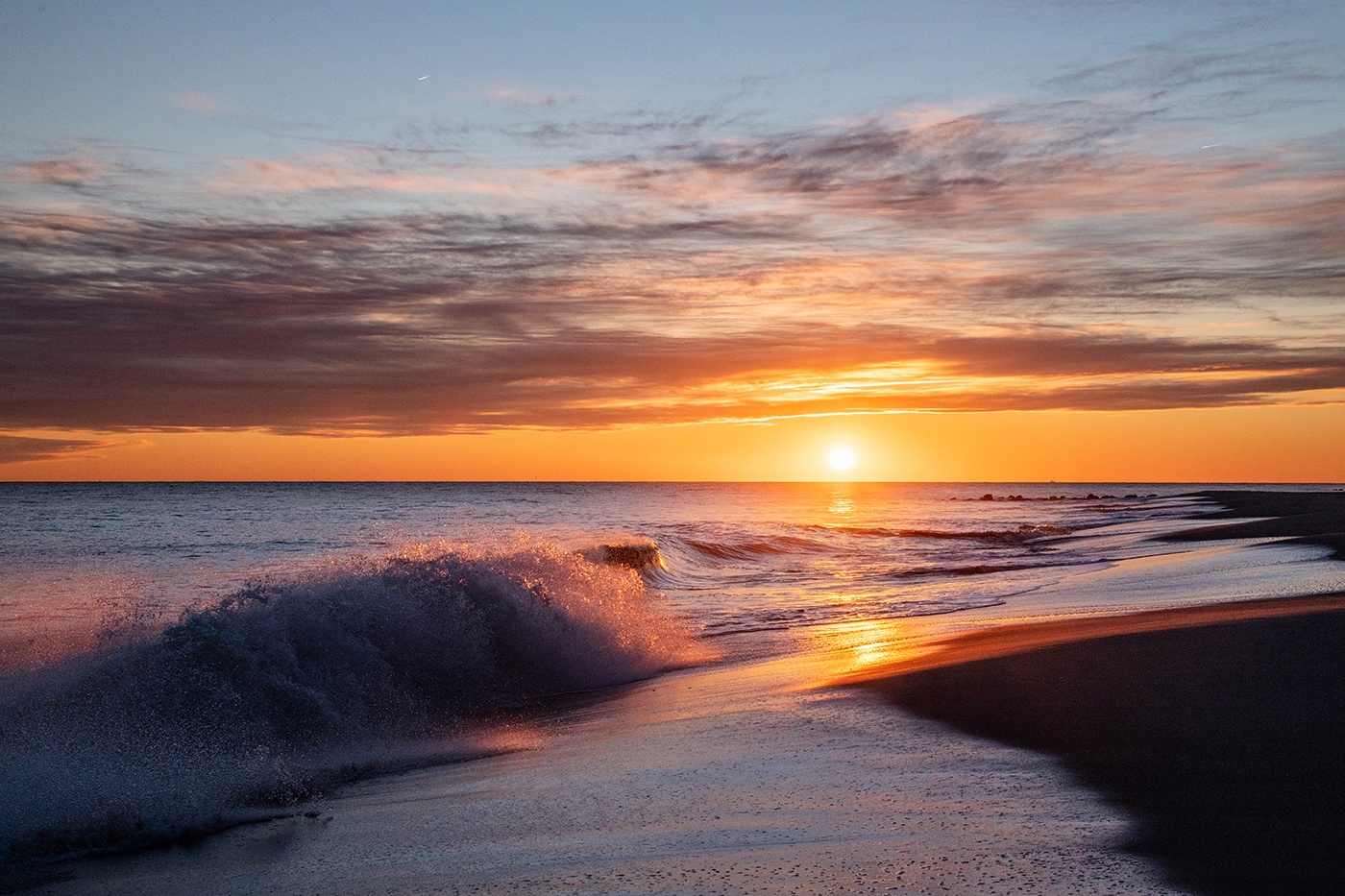 Sun setting with whispy clouds in the sky and waves crashing on the beach