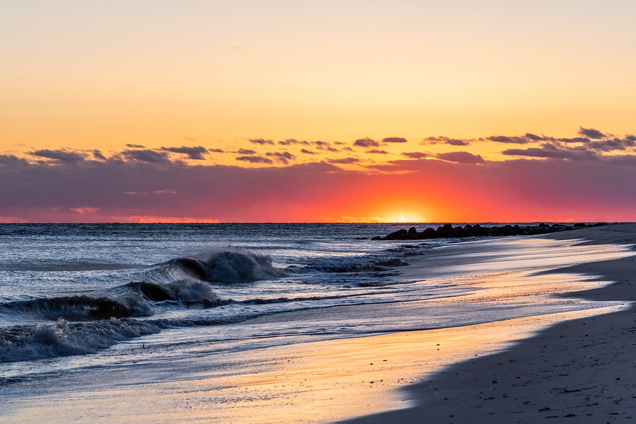 Colorful clouds at the horizon with blue waves crashing at the shoreline