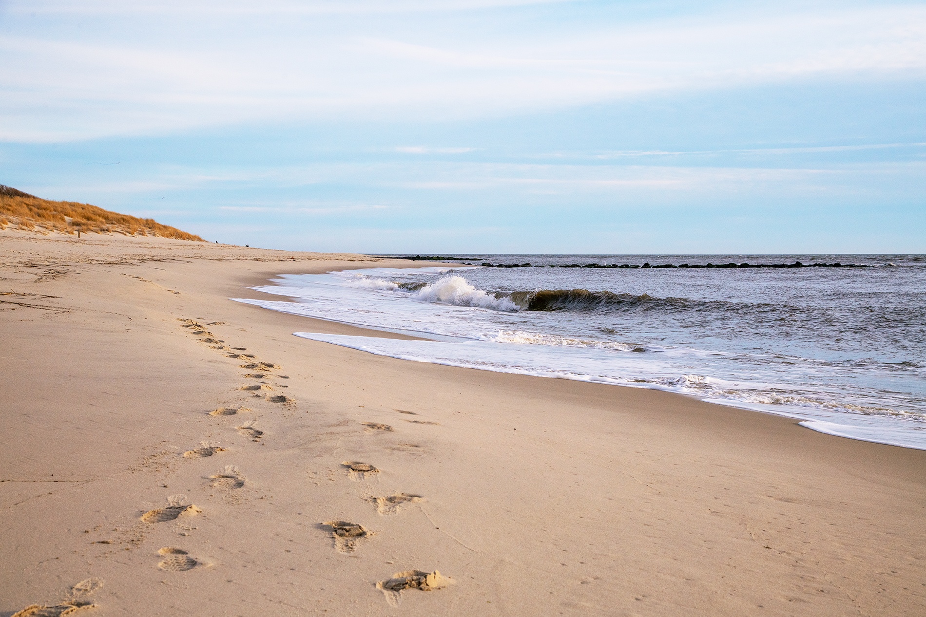 Two pairs of footprints in the sand as a wave crashes on the shore on an overcast day