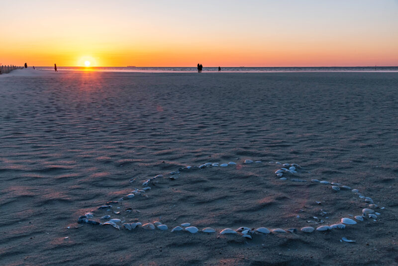 Sunrise at the beach with shells in the form of a heart on the sand