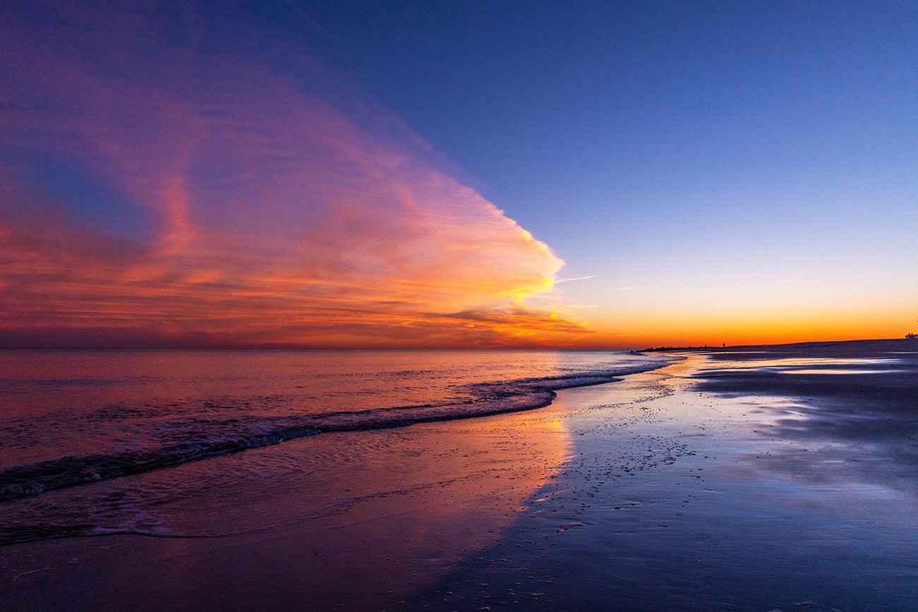 Colorful clouds in the sky at sunset reflected in the ocean and sand