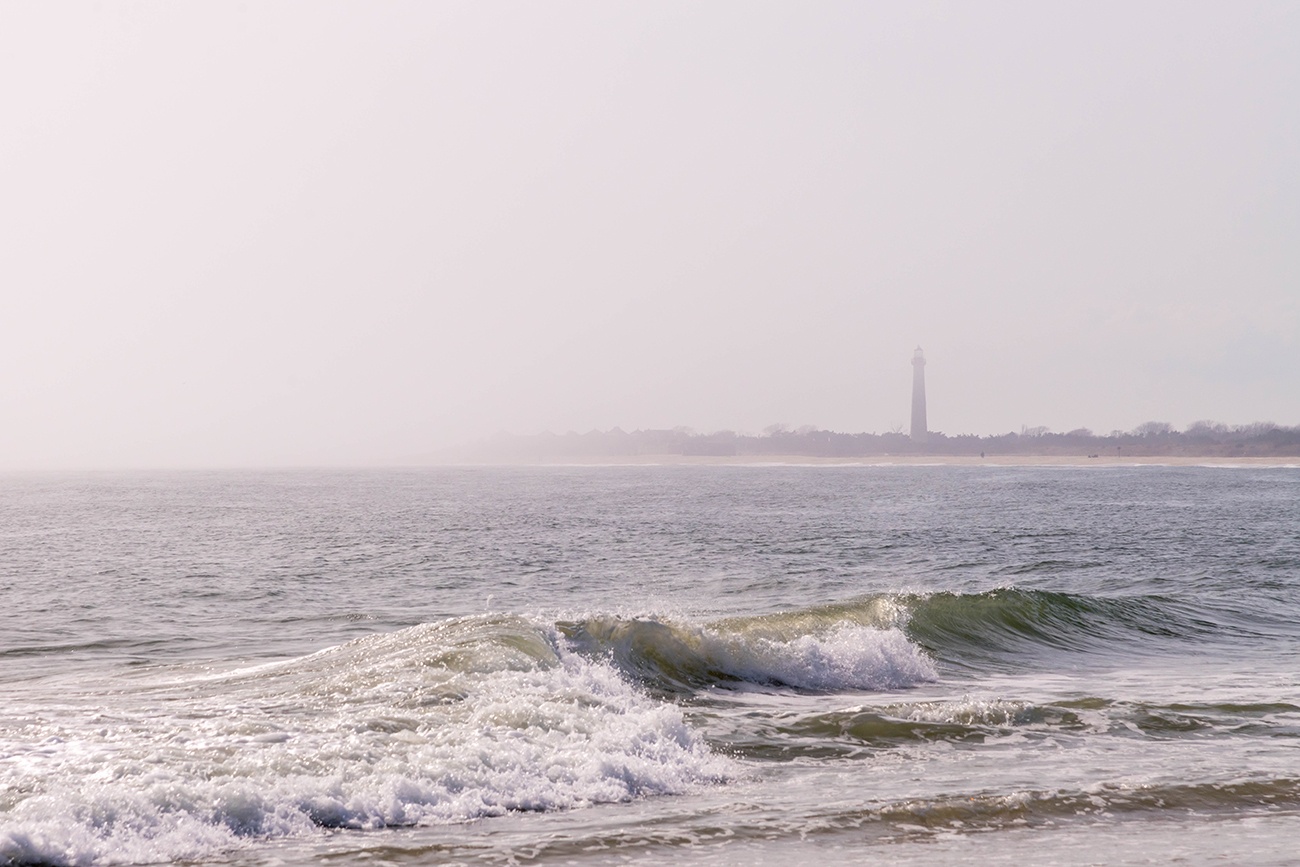 The Cape May Lighthouse in the distance on a foggy day with waves crashing