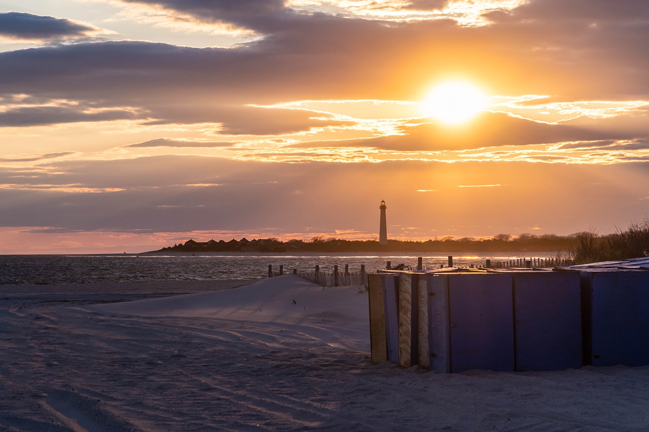 Sun setting behind the Cape May lighthouse with Steger's beach boxes on the beach