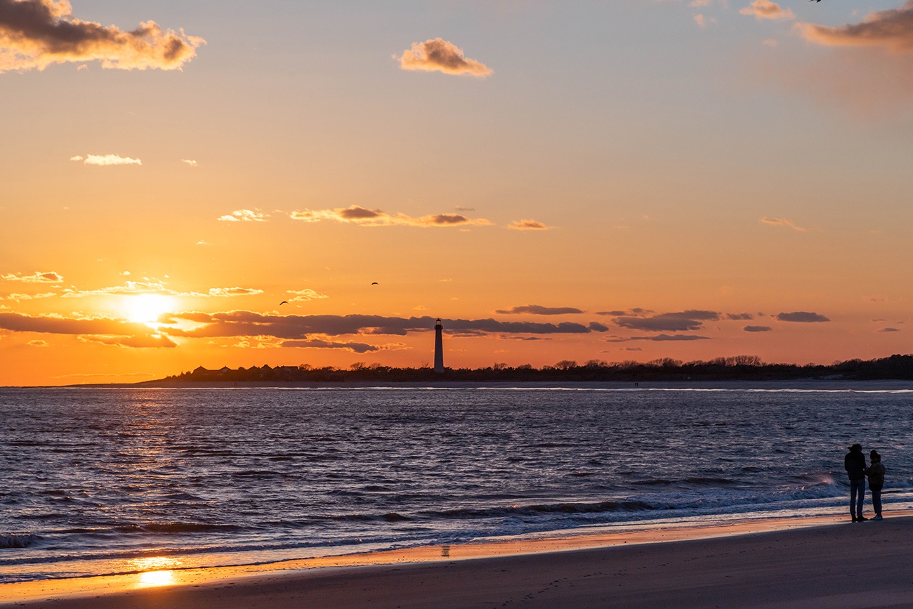 Two people watching the sun set with the Cape May Lighthouse in the distance