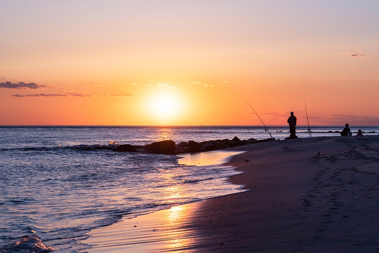 A person fishing at sunset at the beach with waves crashing