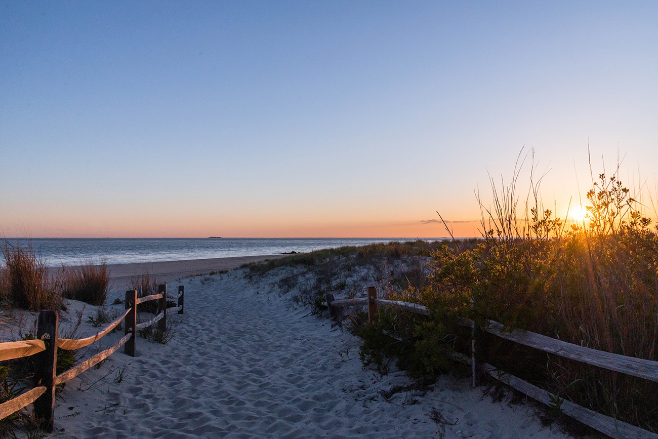 A path entrance to the beach with the sun setting 