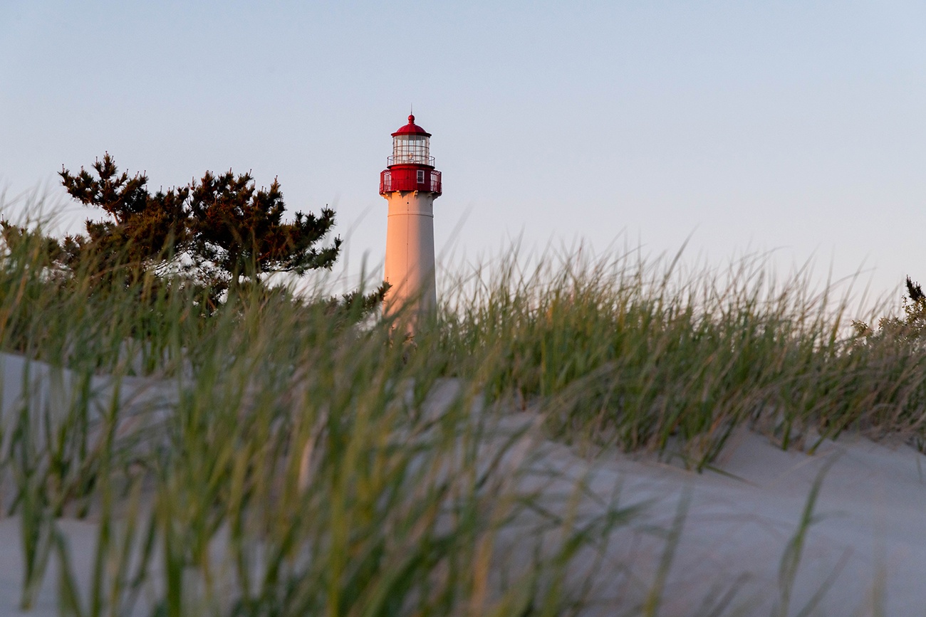 Sunlight on the Cape May Lighthouse with green beach dunes in the foreground