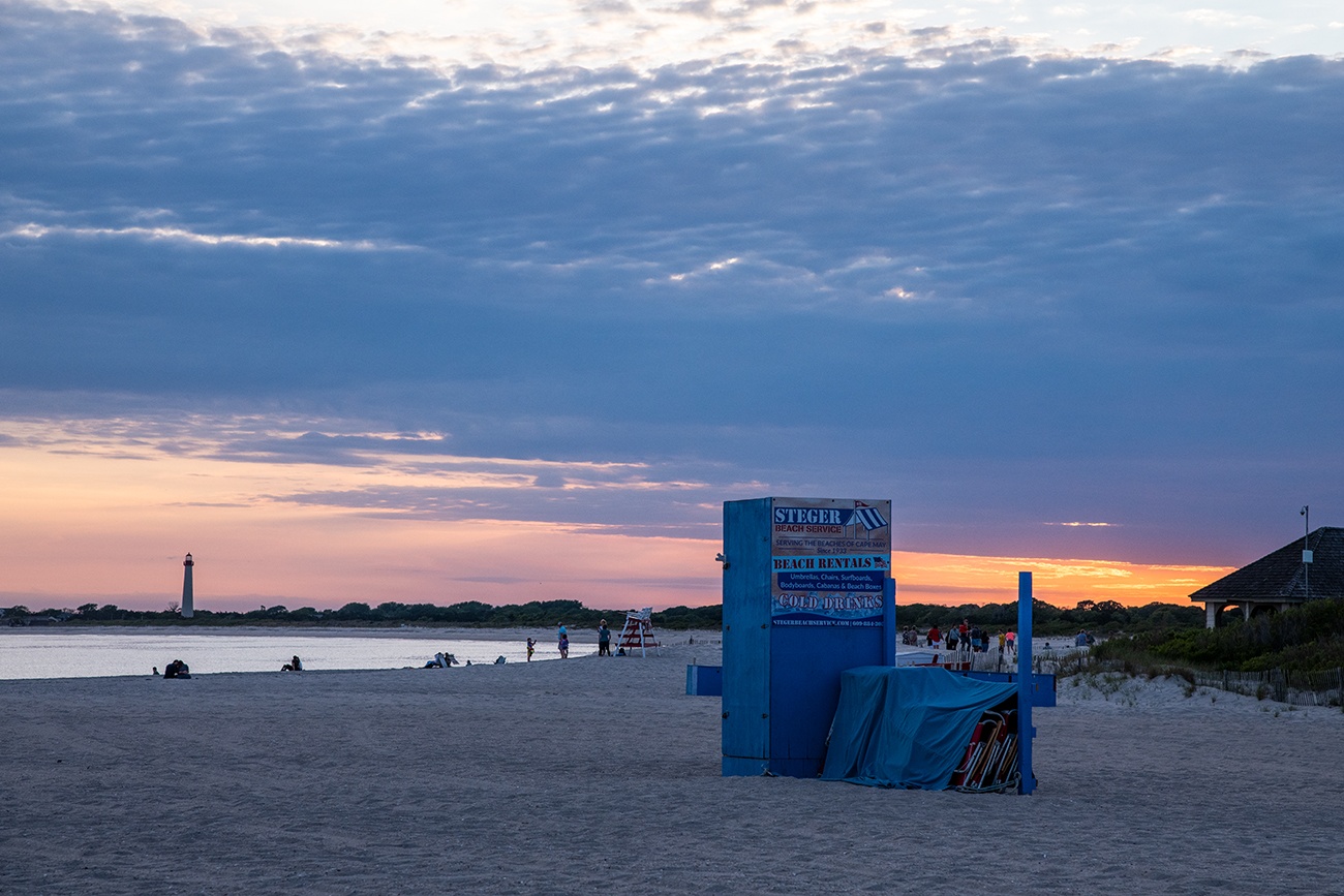 Steger's beach service box and chairs covered up at the end of the day at sunset with the Cape May Lighthouse in the distance