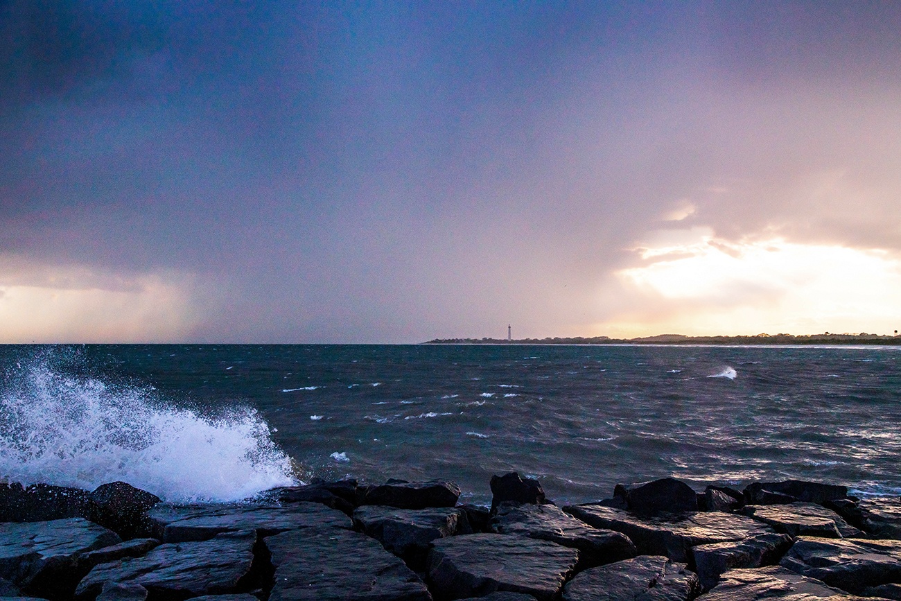 Rain storms at sunset with waves crashing and the Cape May Lighthouse in the distance