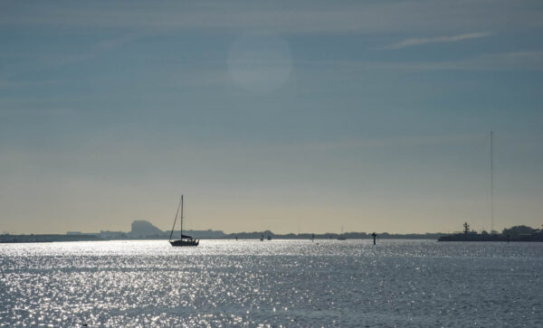 A sailboat sailing away in the Cape May Harbor in the early morning.