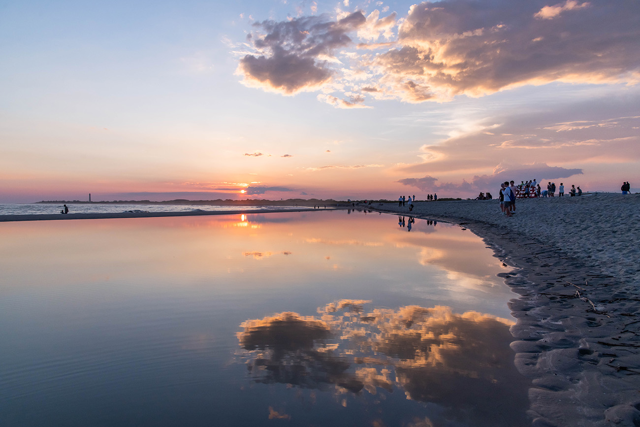 Sunset reflected in a pool of water at the beach with the Cape May lighthouse in the distance