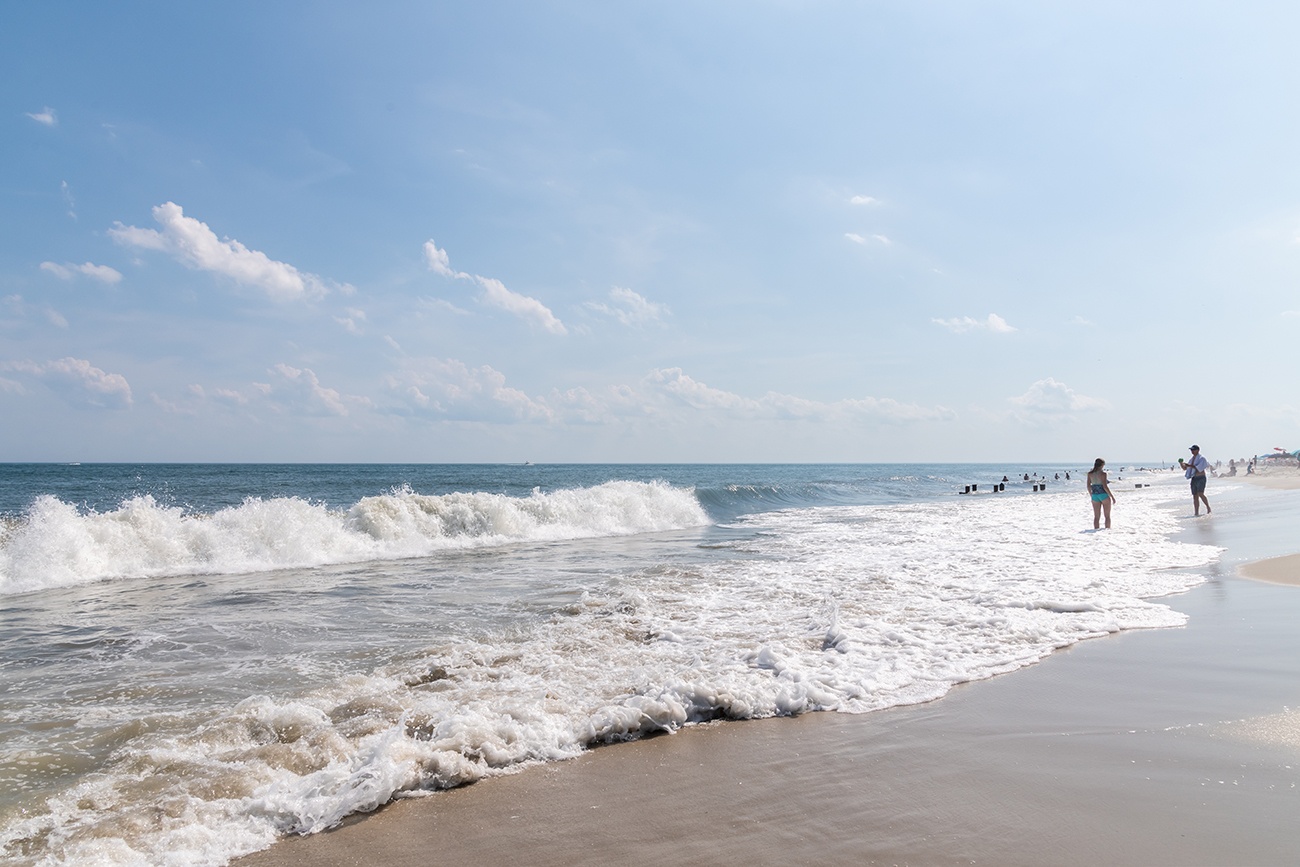 Two people standing at the ocean on a bright blue sunny summer day at the beach