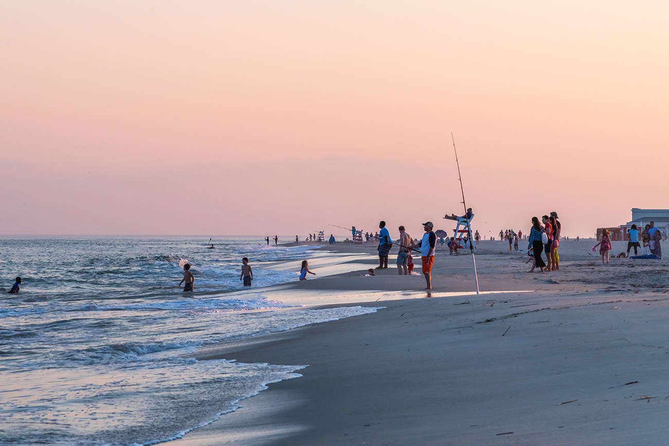 People fishing, swimming, and gathered by the ocean at sunset