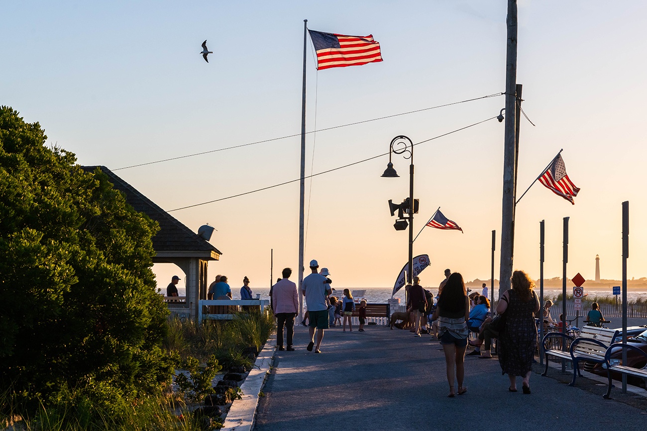 People walking on the promenade at sunset with American flags flying