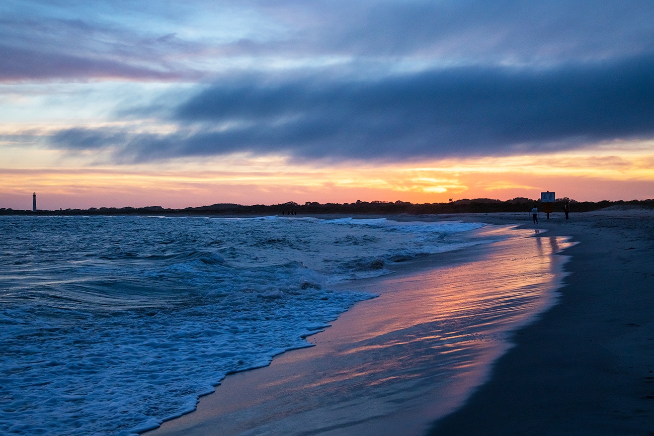 Clouds at the horizon at sunset on the beach with the Cape May lighthouse in the distance