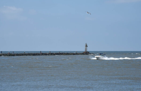 A boat heading back to the harbor, people fishing on the jetty