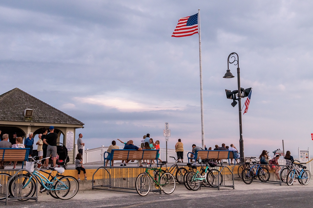 People sitting and bikes lined up at the end of the Promenade with an American Flag waving