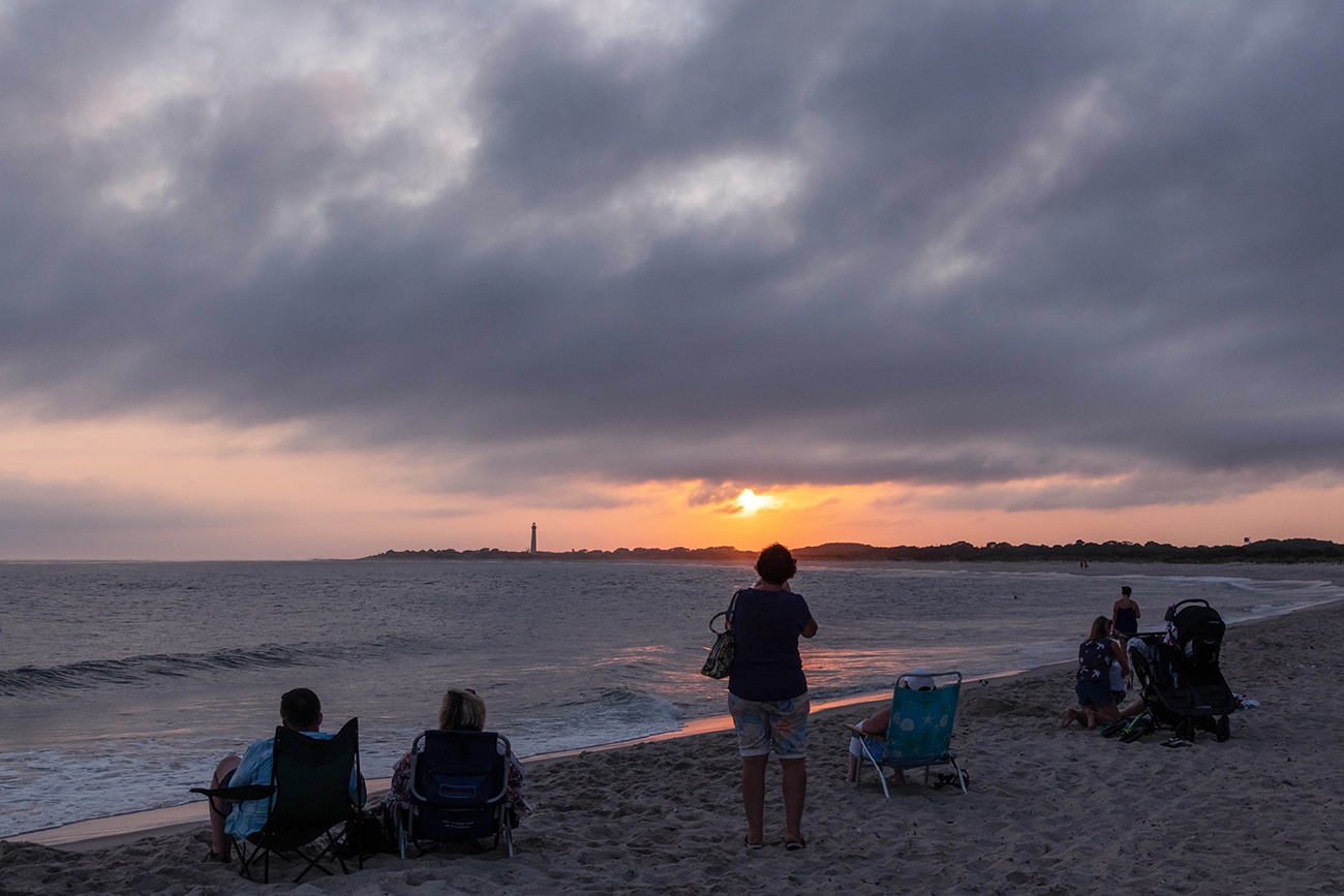 Sun setting with clouds in the sky with people sitting on the beach