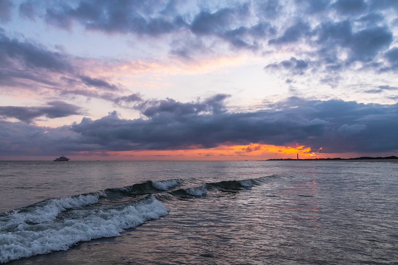 Purple clouds moving in the sky at sunset over the ocean with an orange streak of light at the horizon