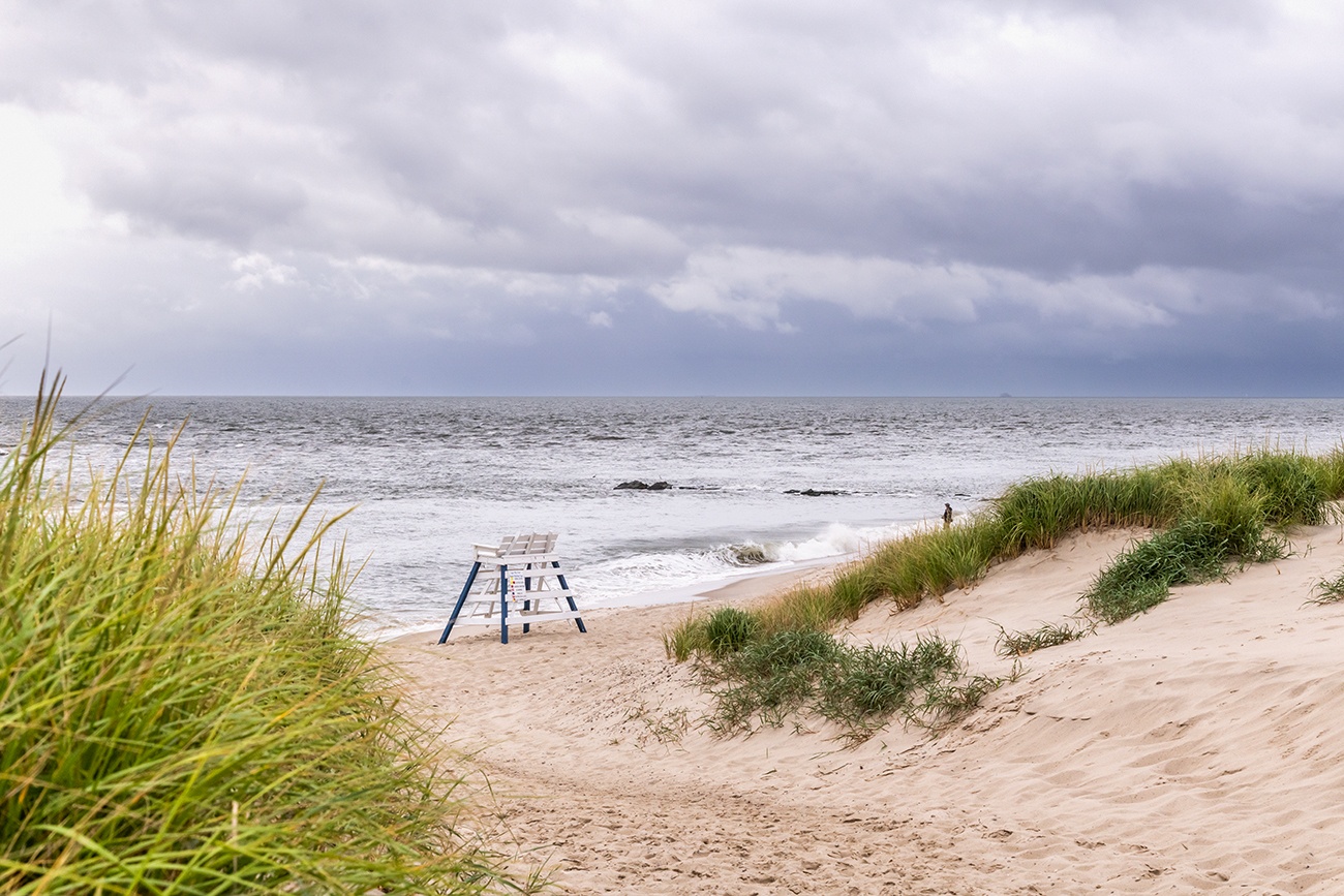 A lifeguard stand at the end of a sand path to the beach with dark clouds in the sky